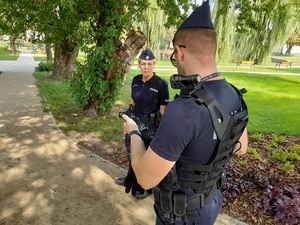 w parku policjant spogląda na trzymany w ręce terminal. Obok stoi policjantka