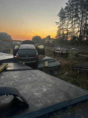 poza jezdnią, na gruntowej nawierzchni, wśród materiałów i sprzętu budowlanego znajduje się rozbity czarny opel astra.