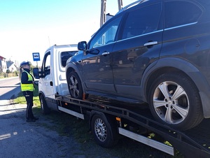 przy kabinie ciężarowego pojazdu z  lawetą, na której znajduje się osobowy chevrolet, stoi policjantka ruchu drogowego