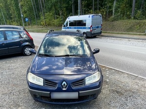 na miejscu parkingowym stoi granatowe renault megane. Za nim na jezdni stoi policyjny radiowóz z włączonymi sygnałami błyskowymi