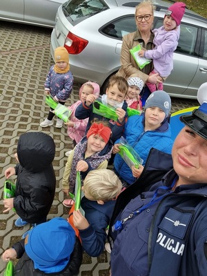 selfie policjantki ruchu drogowego i przedszkolaków trzymających pakiety z elementami odblaskowymi