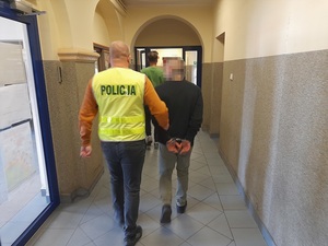 policjant prowadzi korytarzem mężczyznę skutego kajdankami