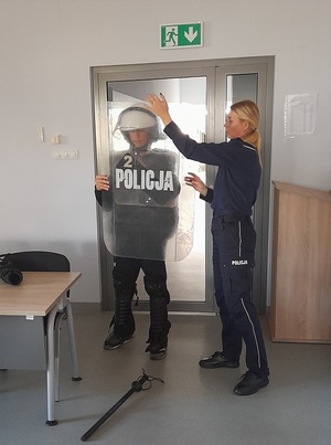 policjantka pomaga uczniowi założyć sprzęt przeciwuderzeniowy