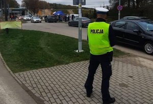 na chodniku w okolicy cmentarza stoi policjant ruchu drogowego, który obserwuje ruch pieszych i pojazdów