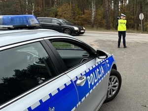 stojąca na poboczu policjantka ruchu drogowego mierzy prędkość przejeżdżającego samochodu za pomocą ręcznego miernika prędkości