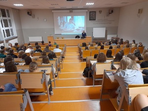 w auli na tle wyświetlanego filmu stoi policjantka z mikrofonem. Przed nią znajdują się uczniowie