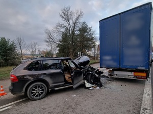 miejsce wypadku drogowego. Na jezdni za przyczepą ciężarówki stoi czarne porsche z wgniecionym przodem