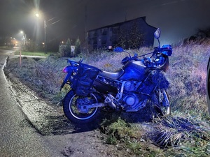 pora nocna. Na poboczu prostopadle do jezdni stoi motocykl z kępami trawy na karoserii.