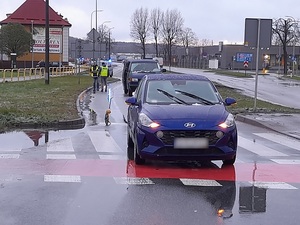 miejsce wypadku drogowego. Dwuetapowe przejście przez pasy. Na pasach przed przejazdem rowerowym stoi niebieski osobowy hyundai. Obok niego stoi urządzenie do pomiaru odległości. Za nim stoi policyjny radiowóz oraz dwaj policjanci