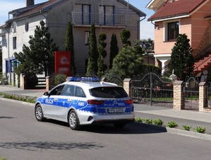 oznakowany policyjny radiowóz na jezdni przy budynkach mieszkalnych