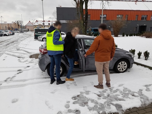 dwaj policjanci po cywilnemu wprowadzają do nieoznakowanego radiowozu zatrzymanego mężczyznę