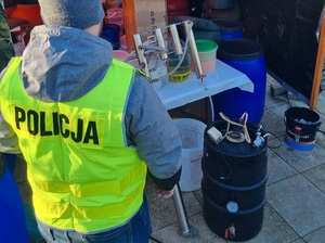 policjant i funkcjonariuszka KAS stoją przed namiotem w którym odbywa się nielegalna produkcja alkoholu