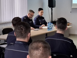 w auli komendy lęborskiej Policji przy stole siedzą prowadzący odprawę Komendant Powiatowy Policji w Lęborku oraz Zastępca Komendanta Wojewódzkiego Policji w Gdańsku