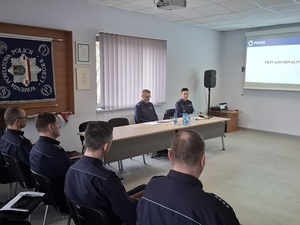 w auli lęborskiej komendy Policji przy stole siedzą prowadzący odprawę Komendant Powiatowy Policji w Lęborku oraz Zastępca Komendanta Wojewódzkiego Policji w Gdańsku