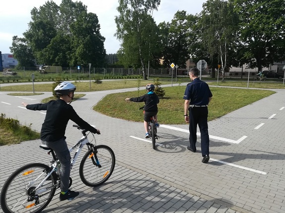 po miasteczku ruchu drogowego w lęborskiej komendzie Policji jedzie dwoje młodych rowerzystów. Przygląda się im policjant