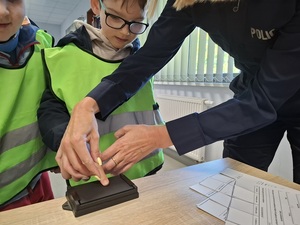 policjantka przykłada palec przedszkolaka do gąbki z tuszem