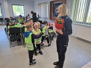 w auli budynku komendy lęborskiej policji policjantka przybija żółwika z przedszkolakiem. W ręce trzyma kwiaty. Przed nimi siedzą pozostałe przedszkolaki