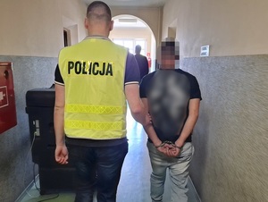 policjant prowadzi korytarzem mężczyznę, który ma ręce skute za plecami kajdankami