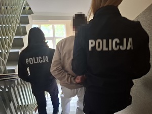 dwie policjantki prowadzą schodami w dół mężczyznę, który ma ręce skute za plecami kajdankami