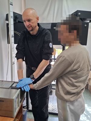technik kryminalistyki skanuje odciski palców zatrzymanego mężczyzny