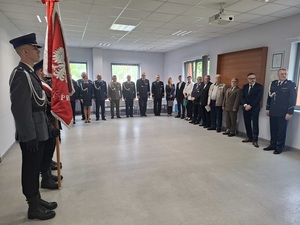 W auli budynku lęborskiej komendy policji stoją obok siebie kadra kierownicza policji, przedstawiciele służb mundurowych, instytucji, władz samorządowych i poczet sztandarowy