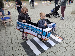 na placu przed policyjnym stoiskiem dwoje dzieci w autochodziku przechodzi przez zabawkowe przejście dla pieszych
