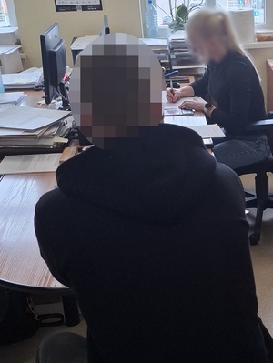 siedząca przed komputerem nieumundurowana policjantka przesłuchuje siedzącego na krześle mężczyznę