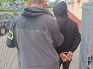 policjant kryminalny wyprowadza z budynku komendy mężczyznę, który ma ręce skute za plecami kajdankami