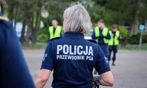grupa policjantów na dworze. Na pierwszym planie policjantka w granatowej koszulce z napisem na plecach &quot;Policja przewodnik psa&quot;
