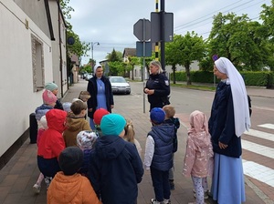 na chodniku przed przejściem dla pieszych stoi grupa przedszkolaków z dwiema siostrami zakonnymi. Przed nimi stoi policjantka, która przemawia do dzieci