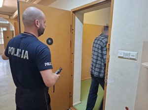 do celi wchodzi zatrzymany mężczyzna. Przy drzwiach celi stoi policjant