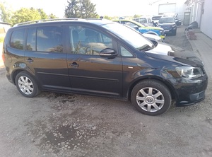 Przed budynkiem na parkingu stoi czarny vw touran. Obok zaparkowanych pojazdów znajduje się policyjny radiowóz