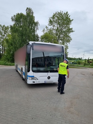 na placu parkingowym policjant ruchu drogowego sprawdza stan techniczny autokaru