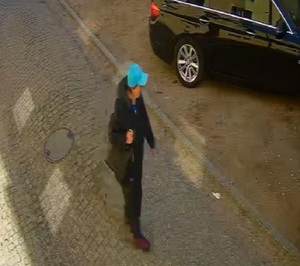 idąca ulicą kobieta w czarnej kurtce, ciemnych spodniach i niebieskiej czapce z daszkiem, z czarną torebką zawieszoną na ramieniu