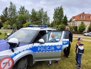 festyn. Do radiowozu przy którym stoi policjant wchodzą dwaj chłopcy