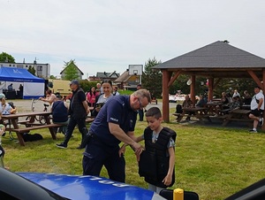 festyn. Policjant pomaga chłopcu założyć kamizelkę przeciwuderzeniową