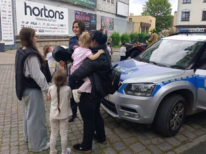 festyn. Przy radiowozie stoi kobieta z dzieckiem na rękach i nastolatka. Rozmawia z nimi policjantka