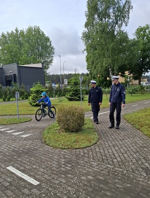 na terenie miasteczka ruchu drogowego dwaj policjanci z drogówki obserwują chłopca jadącego rowerem