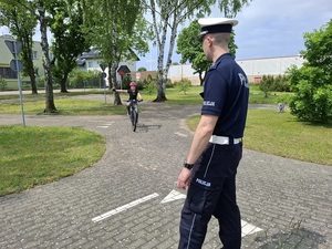 na terenie miasteczka ruchu drogowego policjant z drogówki obserwuje dziewczynkę jadącą rowerem