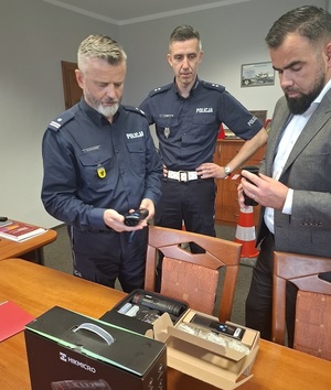 w gabinecie komendanta lęborskiej Policji przy stole stoją: Komendant, Naczelnik Wydziału Ruchu Drogowego i Starosta Lęborski, którzy oglądają trzymane w rękach alkotesty