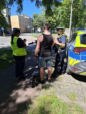 na drodze dla rowerów policjant i policjantka kontrolują młodego mężczyznę, stojącego przy hulajnodze elektrycznej