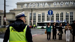 policjant ruchu drogowego na tle budynku dworca w Gdyni Głównej. Przed nim stoi grupa młodych ludzi