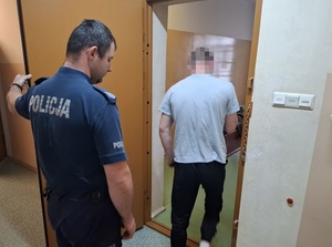 do celi wchodzi mężczyzna. Za nim stoi policjant, który przytrzymuje drzwi celi
