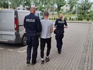 policjant i policjantka prowadzą zatrzymanego mężczyznę w kierunku nieoznakowanego radiowozu