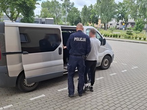 przed otwartymi bocznymi drzwiami nieoznakowanego radiowozu stoją zatrzymany mężczyzna i policjant, który przytrzymuje go za ramię