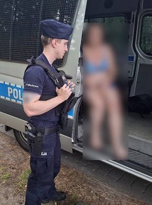 w radiowozie siedzi kobieta w stroju kąpielowym. Obok niej stoi policjant