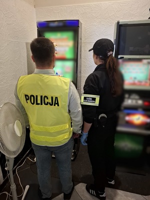 w pomieszczeniu, przed automatem do gier, stoją funkcjonariuszka KAS i nieumundurowany policjant w kamizelce odblaskowej z napisem policja