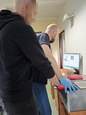 technik kryminalistyki przykłada dłoń zatrzymanego mężczyzny do skanera linii papilarnych