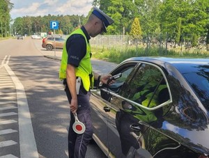 policjant ruchu drogowego sprawdza za pomocą alkomatu trzeźwość kierowcy siedzącego w samochodzie