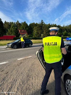policjantka ruchu drogowego sprawdza trzeźwość siedzącego w samochodzie kierowcy. Na poboczu przy radiowozie stoi policjant